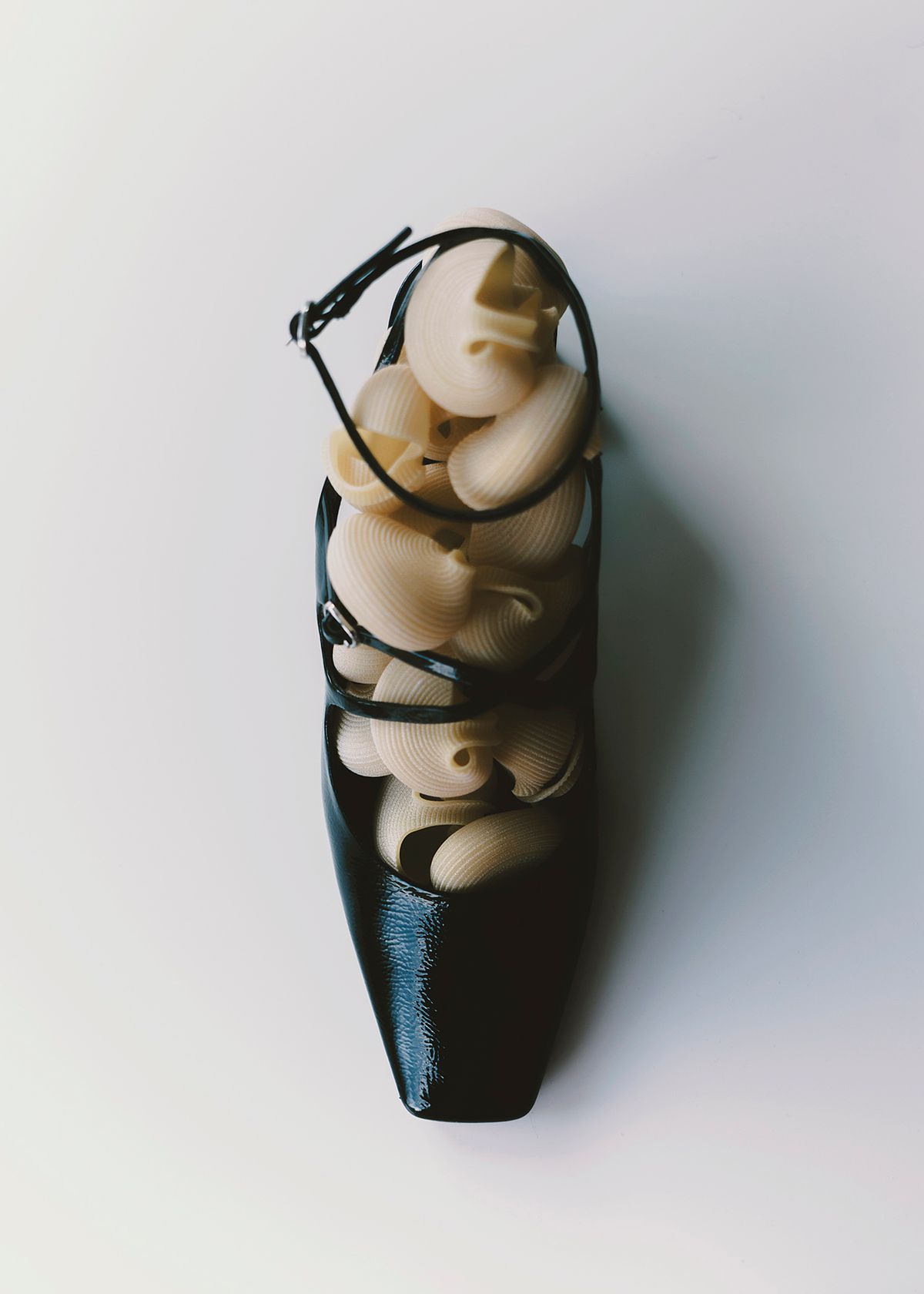 Editorial photo of black pump heeled shoe with straps decorated with pasta props. Photographed by Filianna Karamanli.