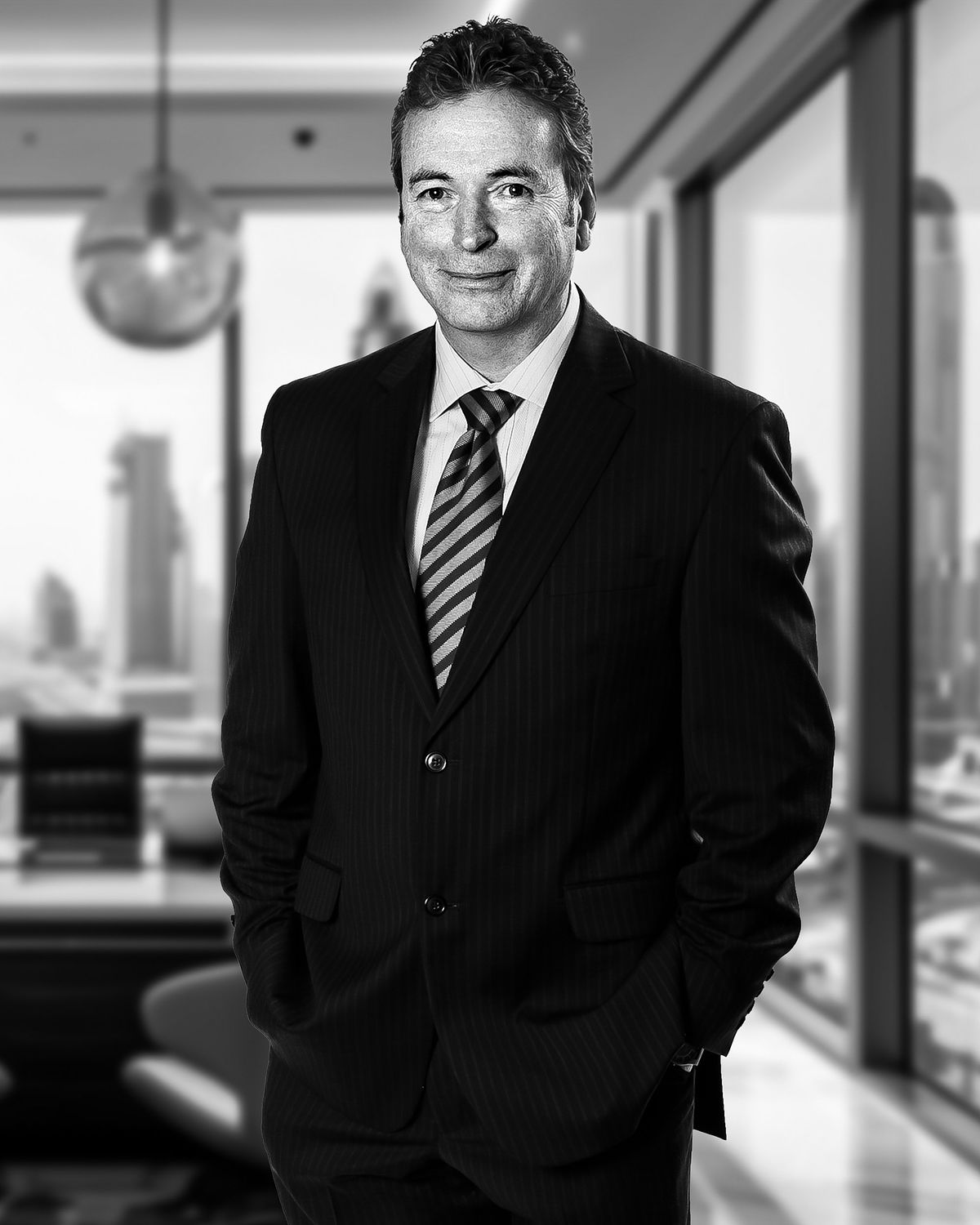 Corporate portrait of an insurance business man in his office. He wears a black suitm white shirt and tie. CIty in the background.