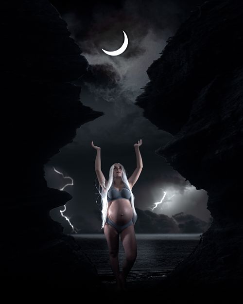 Creative maternity portrait of a woman worshipping the moon during a storm.