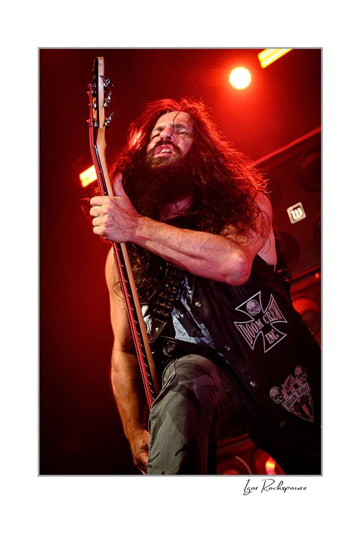 Vertical shot of John JD DeServio standing on stage with his instrument under red lighting.