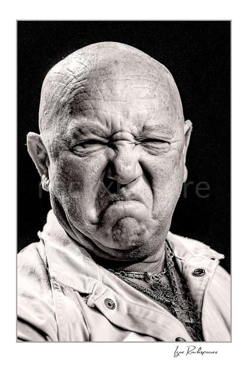 Vertical black and white image of Angry Anderson of Rose Tattoo in a tight onstage close-up with a fierce expression
