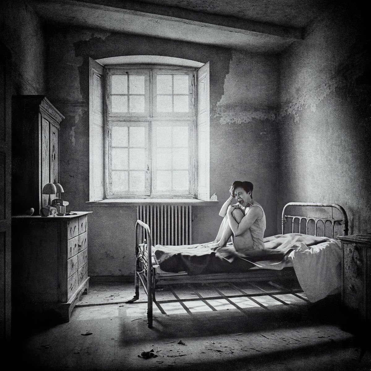 photo tarot The Asylum, femme en camisole hurlant dans une chambre sombre d’asile ancien, éclairée par une lumière crue