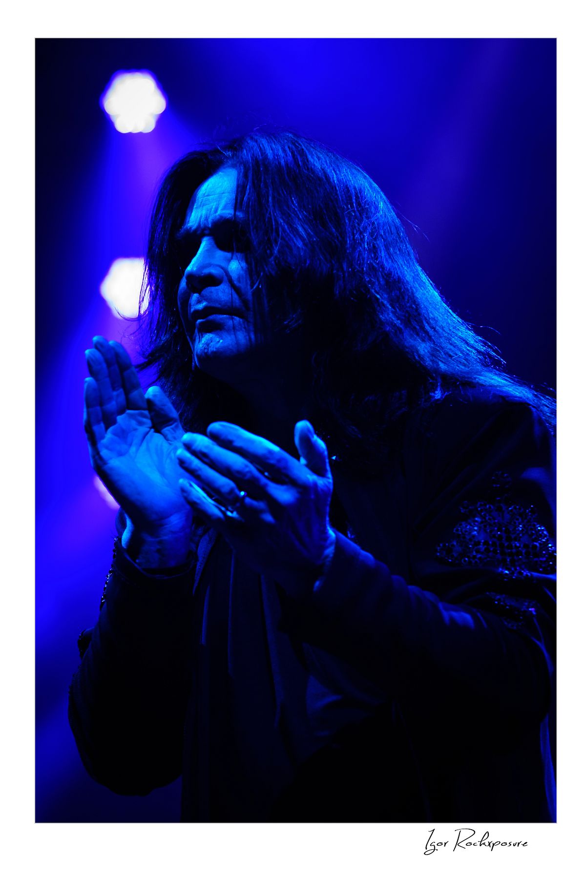 Ozzy Osbourne of Black Sabbath illuminated by deep blue stage lighting holding a microphone during a live performance