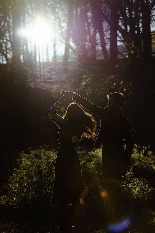 Coppia che danza in controluce nel sottobosco marchigiano, flare di luce e atmosfera giocosa.