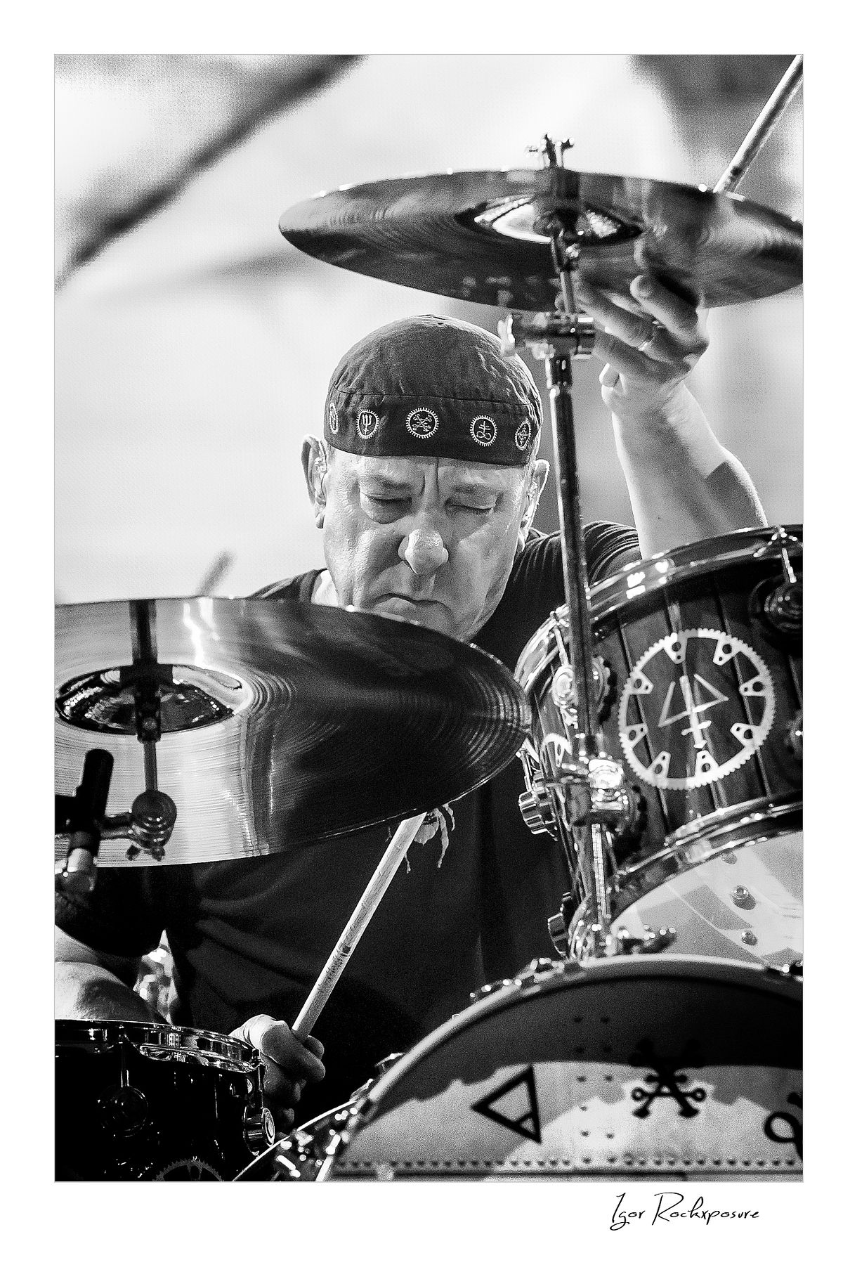 Vertical concert photography of Neil Peart playing drums in black and white photography surrounded by cymbals under stage lighting