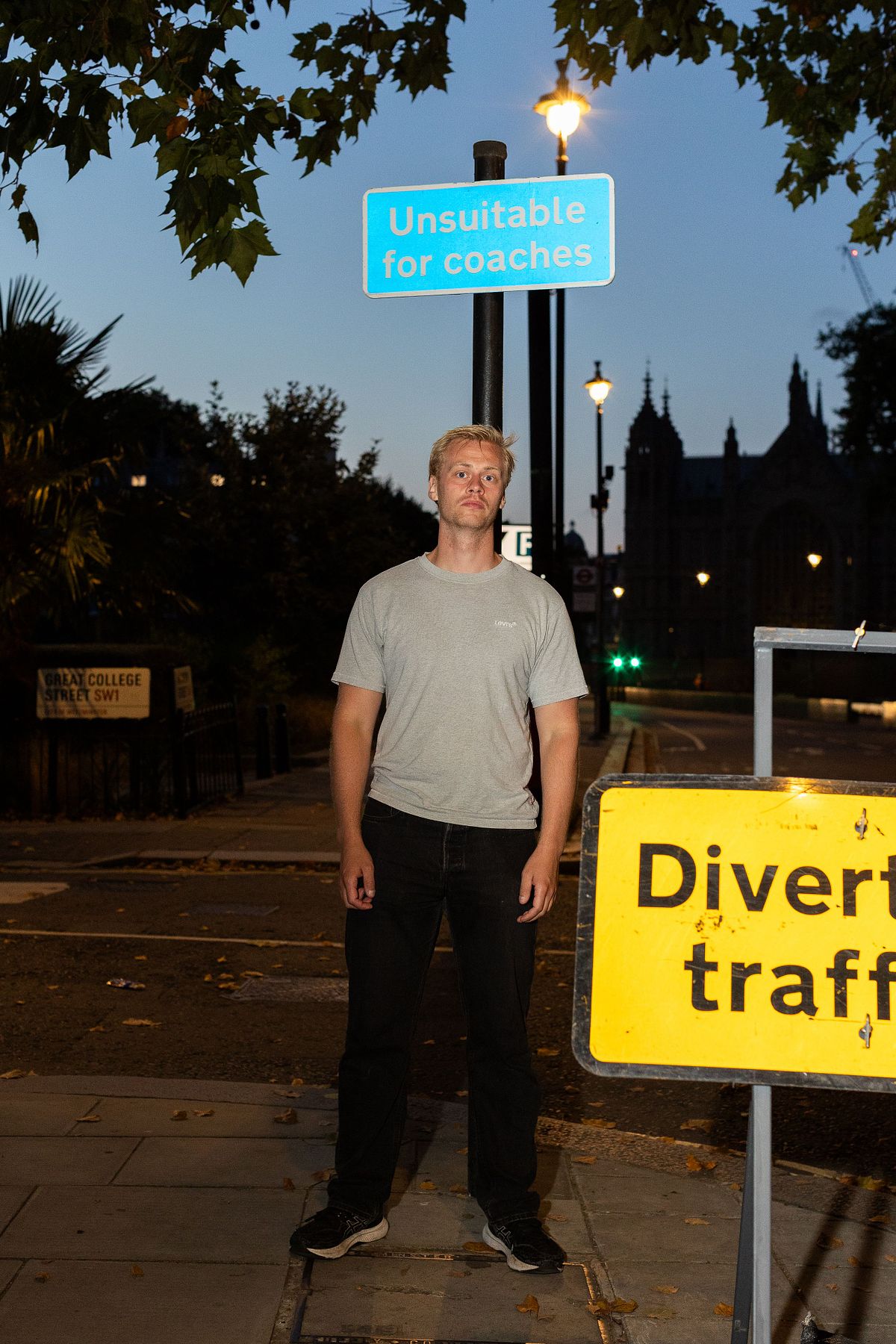Nattligt milj&ouml;portr&auml;tt av en man vid v&auml;gskyltar i London, belyst med blixt, med m&ouml;rk stadsmilj&ouml; och gatljus i bakgrunden.