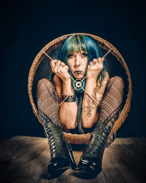 Portrait artistique d’une femme aux cheveux colorés accroupie dans un abat-jour, symbolisant l’enfermement psychologique, la prison mentale et la lutte pour se libérer — œuvre de Pascal Yennis, Namur, Belgique.