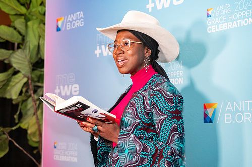 Dr. Joy Buolamwini reading from Unmasking AI during a featured session at Grace Hopper Celebration 2024 in Philadelphia, captured by professional event photographer.