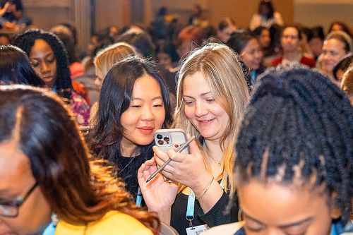 Two attendees sharing a joyful moment during a session break at Grace Hopper Celebration 2024 in Philadelphia, captured by professional event photographer.