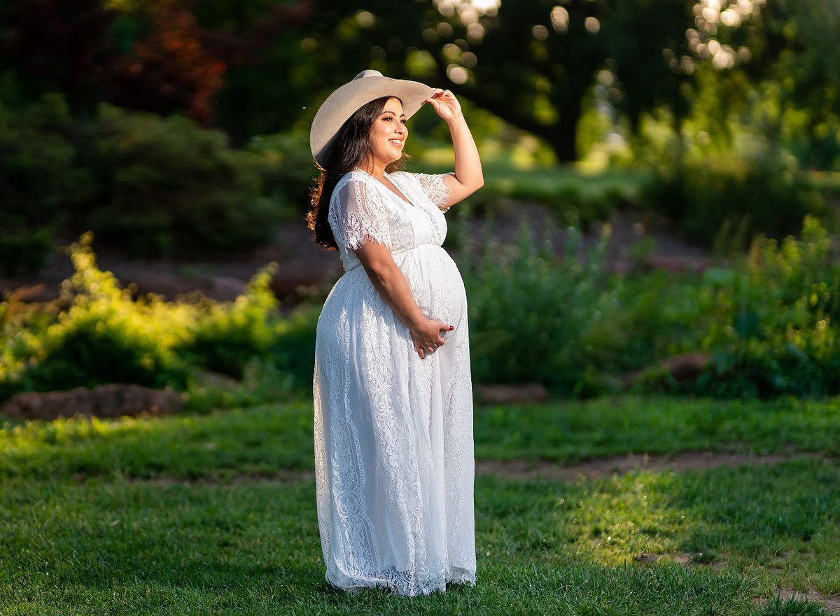 Pregnant woman posing in natural light with a flowing maternity gown.