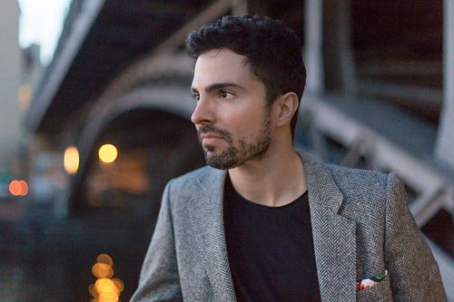 Headshot of Toni Gojanovic in a gray jacket standing near a bridge in Berlin.