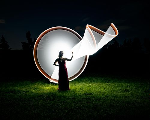 Grad portrait of a young woman standing in front of a light painted circle with a ribbon of light extending out.