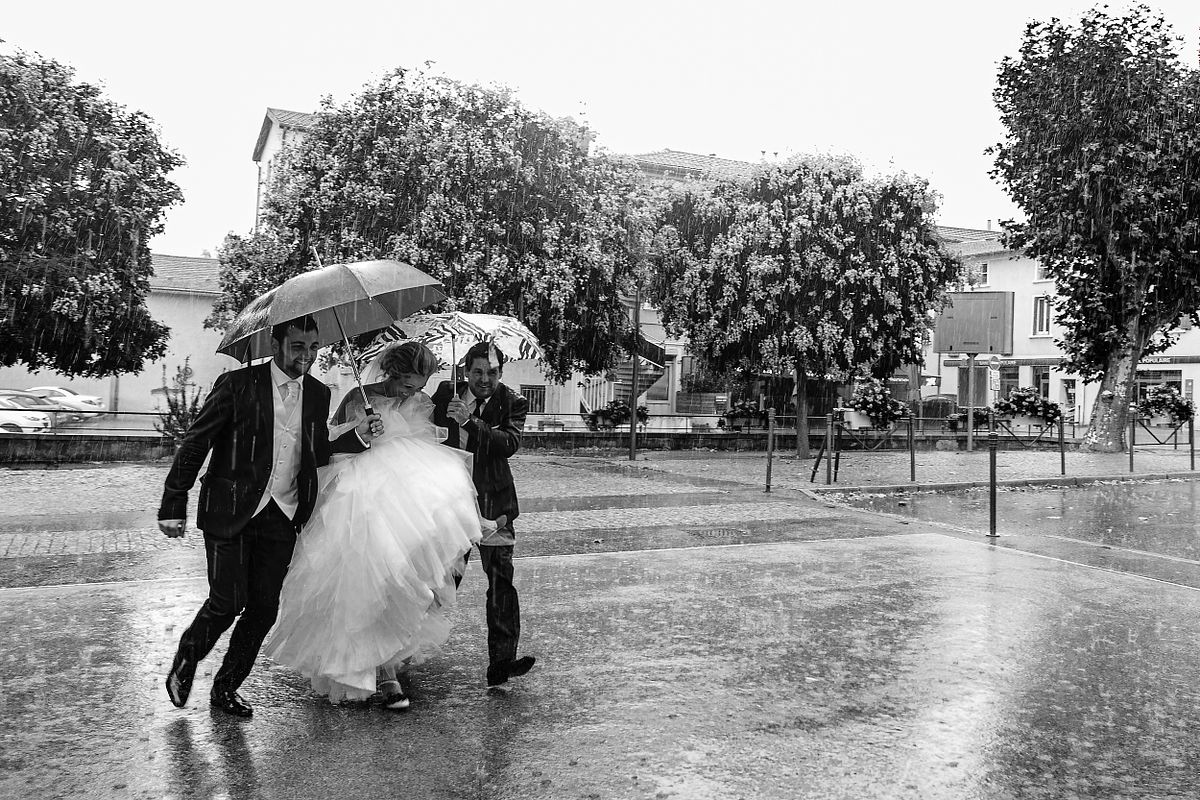 Tarif Photographe Mariage - Sebastien CLAVEL Photographe - Mari&eacute;s sous la pluie, la mari&eacute;e tenue par le mari&eacute; et son p&egrave;re sous des parapluies, rires et amour malgr&eacute; le mauvais temps