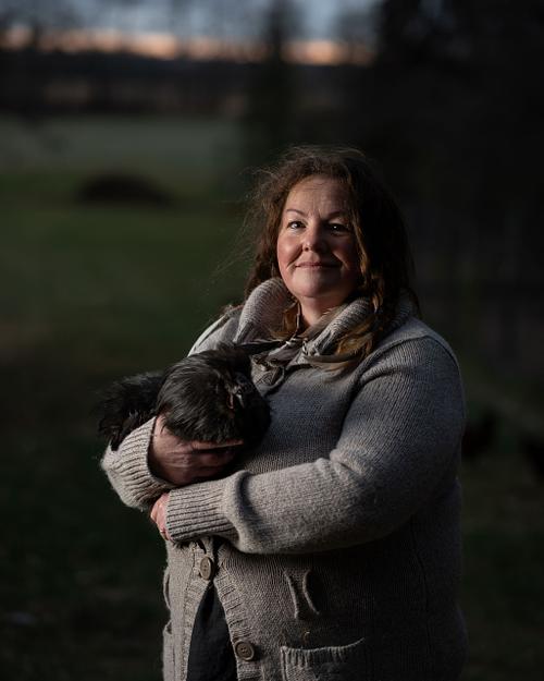 A woman proudly holds her chicken on her farm.