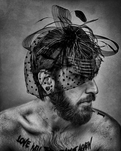Portrait en noir et blanc d&rsquo;un homme barbu et tatou&eacute; portant une voilette d&eacute;licate, exprimant la tendresse masculine assum&eacute;e et la libert&eacute; d&rsquo;identit&eacute; &mdash; photographie fine art par Pascal Yennis, Namur, Belgique.
