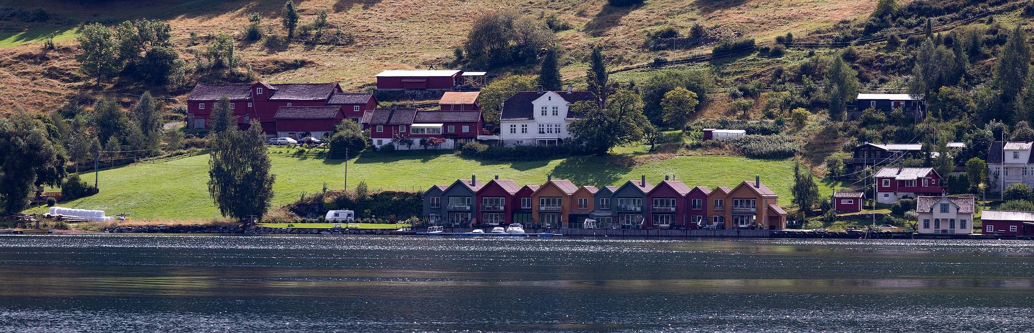 Hameau scandinave au bord de l’eau, reliefs en arrière-plan.