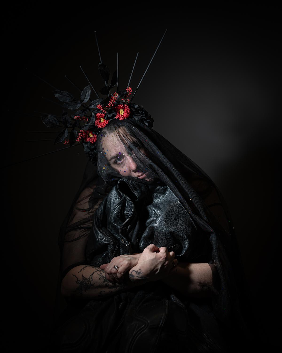 A portrait of a veiled and crowned widow hugging a leather jacket.