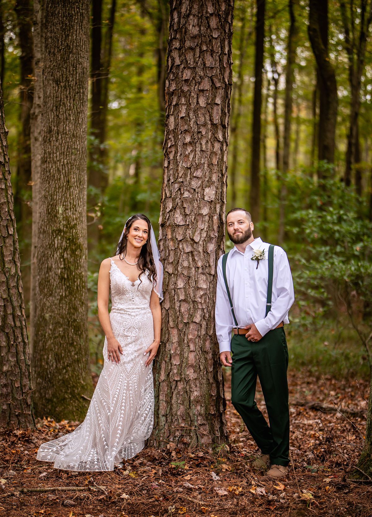 The newly wed couple is posing by a tree in their forest after the wedding ceremony