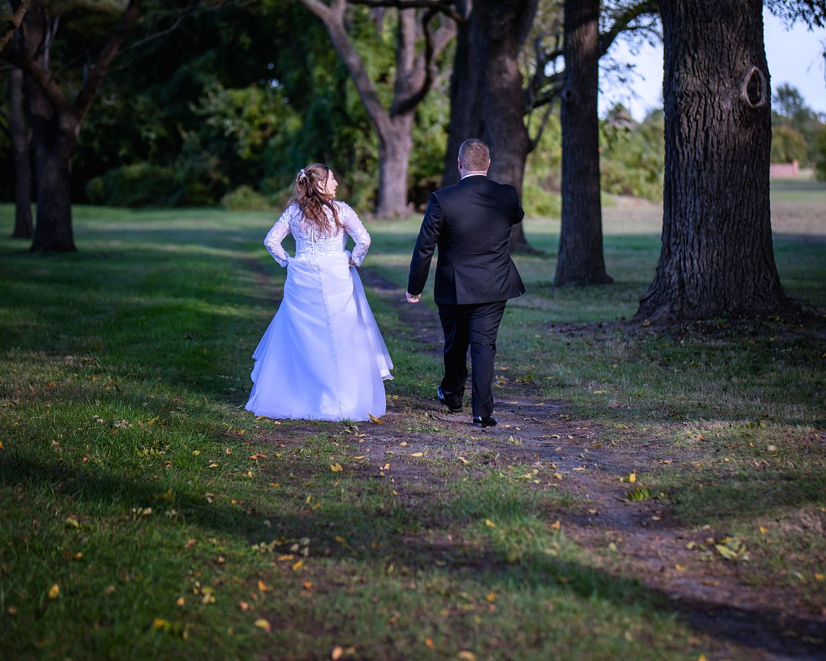 candid moment as a couple walks on the pathway beneath the trees at park at ross mansion for golden hours photography