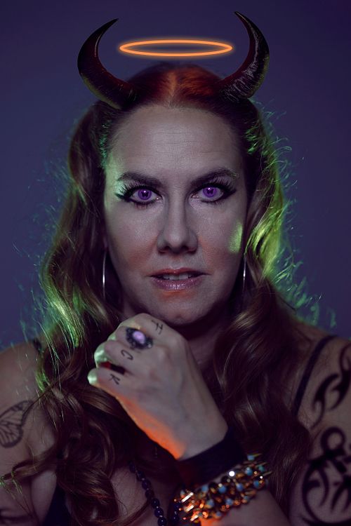 A portrait of a woman with tattoos, devil horns, a halo and butterfly pupils.