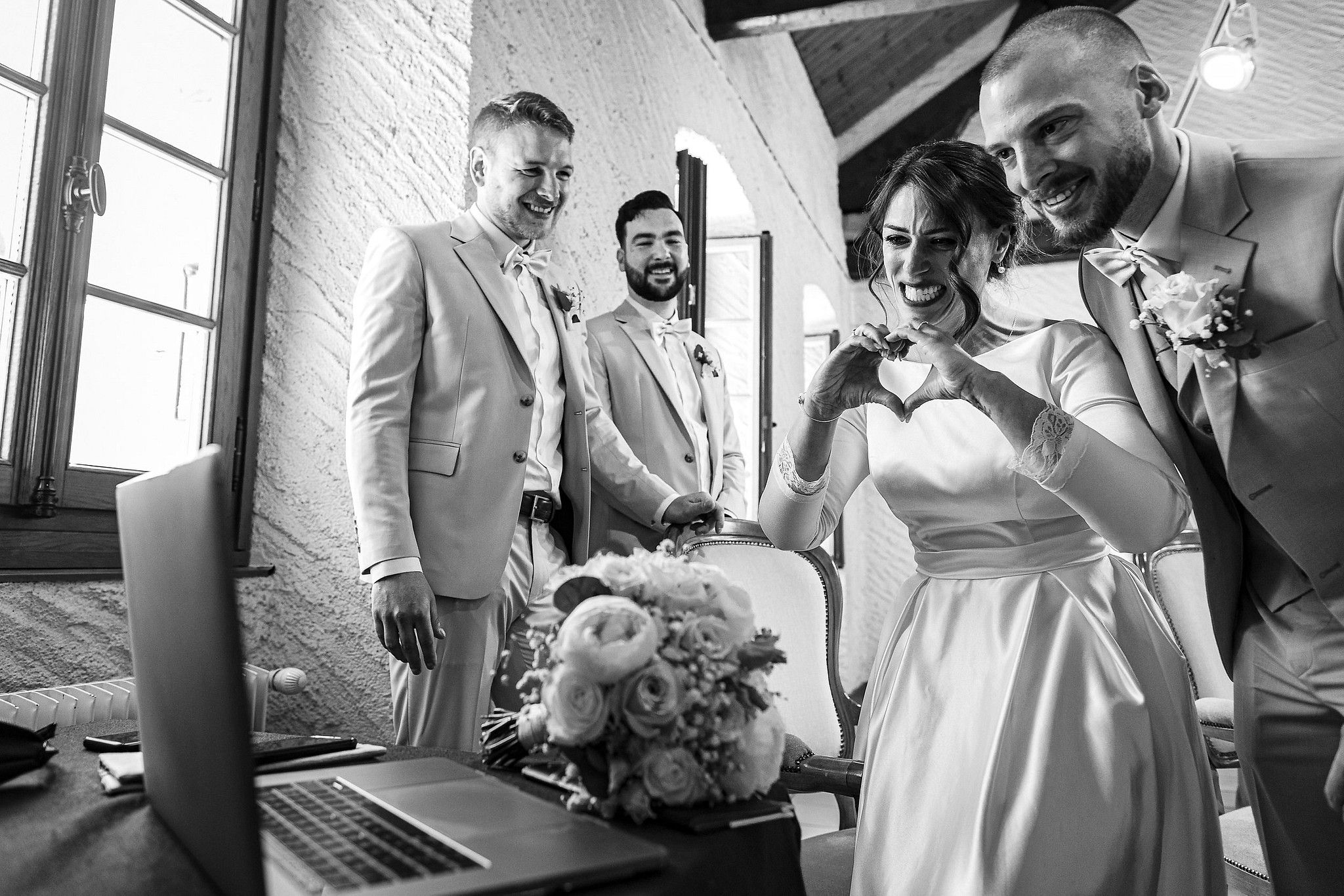 Couple de mari&eacute;s qui font un c&oelig;ur avec leurs mains en regardant un &eacute;cran captur&eacute; par S&eacute;bastien CLAVEL photographe de Mariage &agrave; Lyon et Gen&egrave;ve