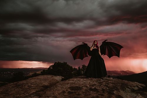 Empowering stormy-day portrait with woman wearing wings on a rugged mountain slope.