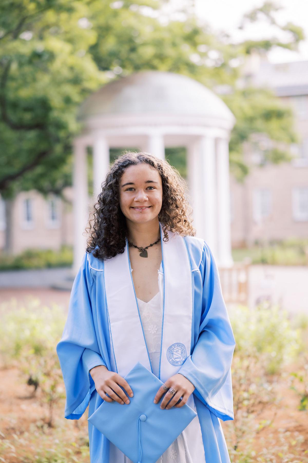 A woman in her graduation robe and stole at the Old Well on UNC's campus in Chapel Hill, NC
