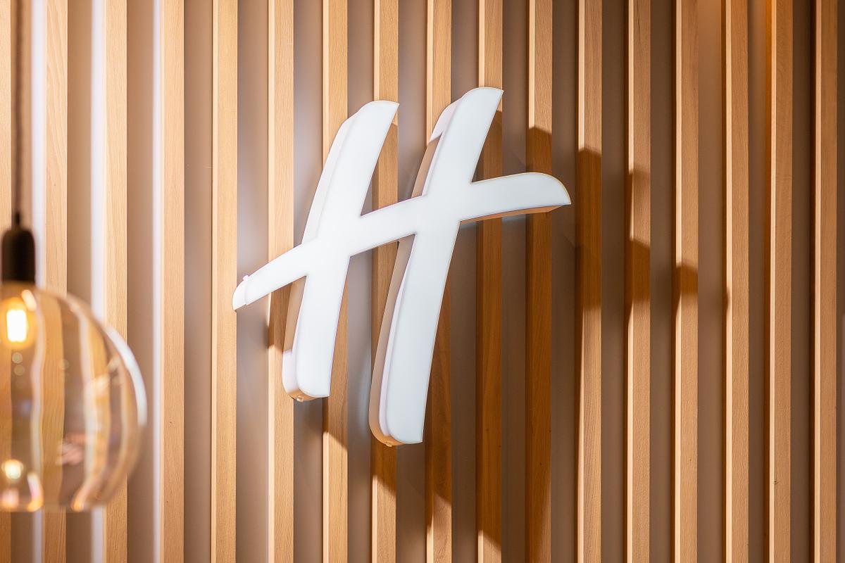 Close-up detail of the Holiday Inn logo, mounted on a vertically slatted wooden wall behind the reception desk at the Holiday Inn Dublin Airport, an IHG Hotel.