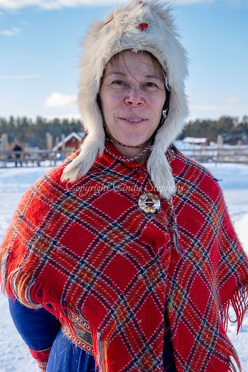 Kristi, a Lapp woman in traditional attire, stands gracefully amid reindeer on a farm in Levi, Finland, showcasing the rich Sami culture.