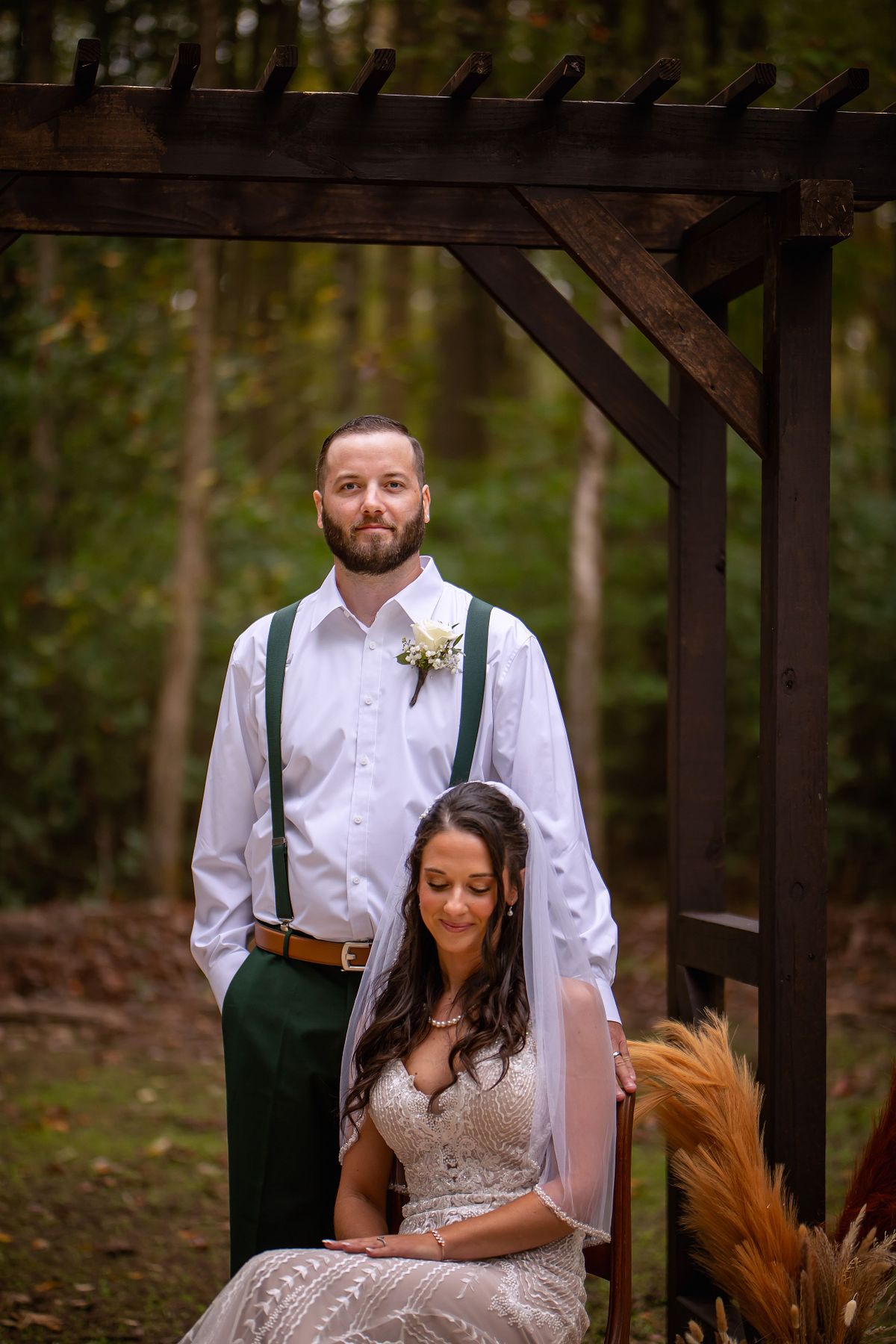Eastern Shore Forest wedding with couple posing under the arbour the groom is standing the bride is sitting on a chair