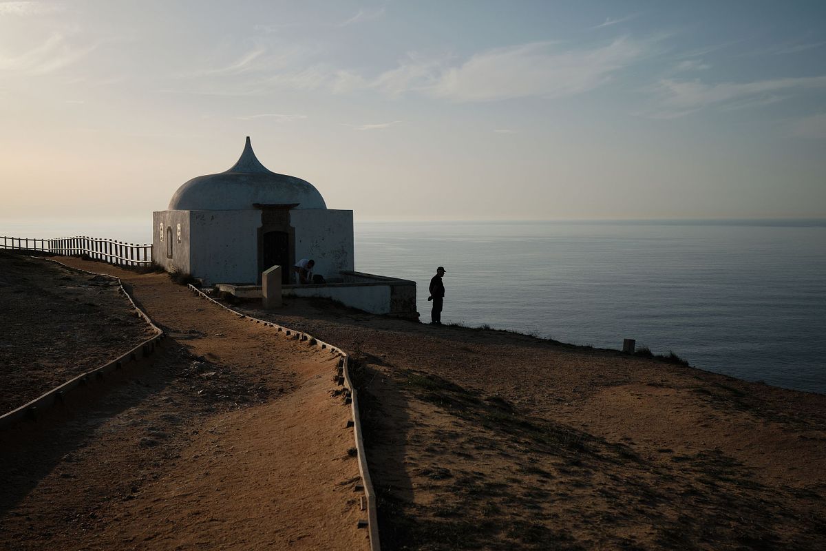 Person standing near a white structure on a cliff overlooking the sea in Portugal, captured by photographer Sandeep Gajula