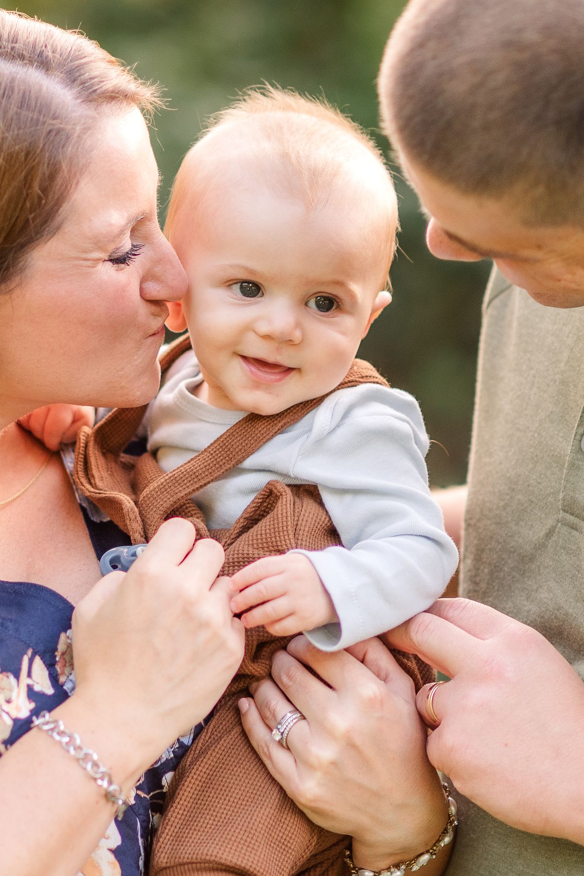 Husband and wife holding their smiling baby and mom gives him a kiss
