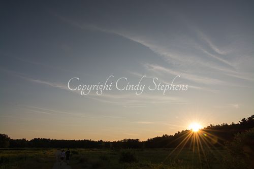 Couple walking at sunset across a meadow with a hilltop
