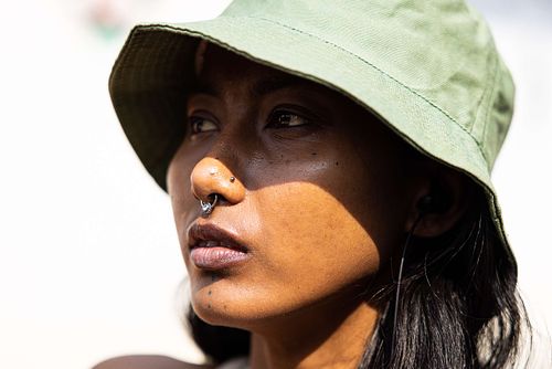 A headshot of an Indian woman with a nose ring, wearing a green bucket hat on a sunny day.