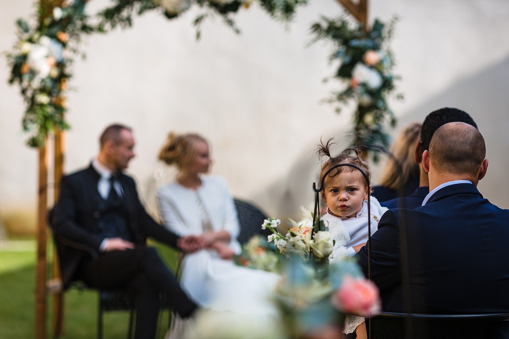 Enfant pendant la c&eacute;r&eacute;monie qui regarde le photographe avec une grimace captur&eacute; par S&eacute;bastien CLAVEL photographe de Mariage &agrave; Lyon et Gen&egrave;ve