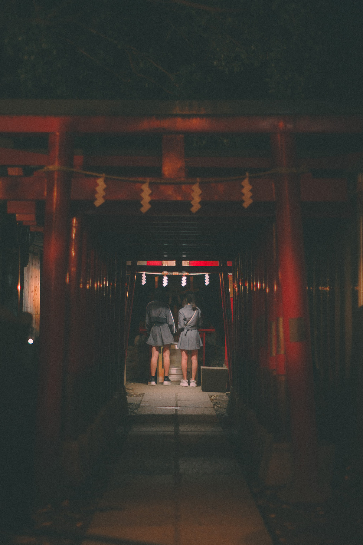 Allée de torii rouges du Hanazono Shrine la nuit, deux visiteuses au fond