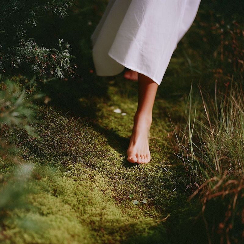close up of a women wearing a white dress in bare feet walking down a mossy path for menopause wellness