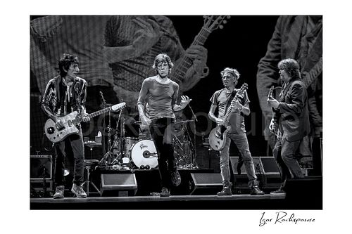 Horizontal black and white image of Ronnie Wood, Mick Jagger, Keith Richards and Mick Taylor of The Rolling Stones performing together on stage