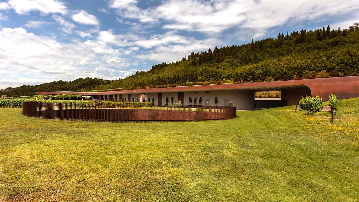 Panoramic view of the Antinori winery in Tuscany, showing its vineyard-covered roof and modern architectural slits integrated into the rolling Chianti hillside.