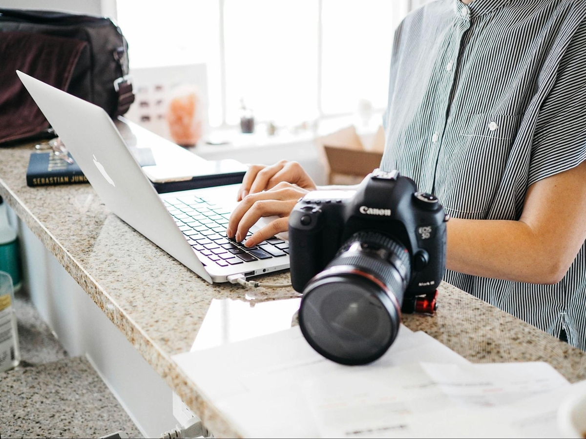een persoon die typt op een laptoptoetsenbord met een Canon-camera bovenop de marmeren tafel