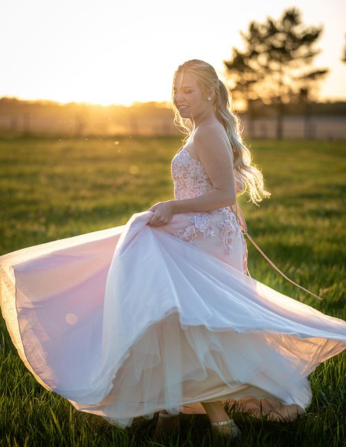 Portrait of graduating student in a pink dress twirling in a field during golden hour.