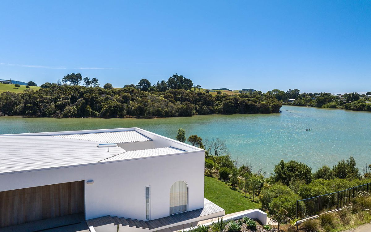 Cinematic aerial drone photography of a modern waterfront residence overlooking the Raglan estuary by Flax Cove Studio.
