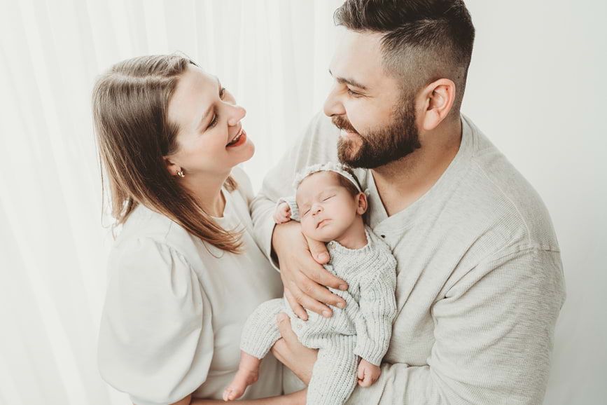 Newborn baby embraced by both parents in a soft-lit studio portrait session in Houston.