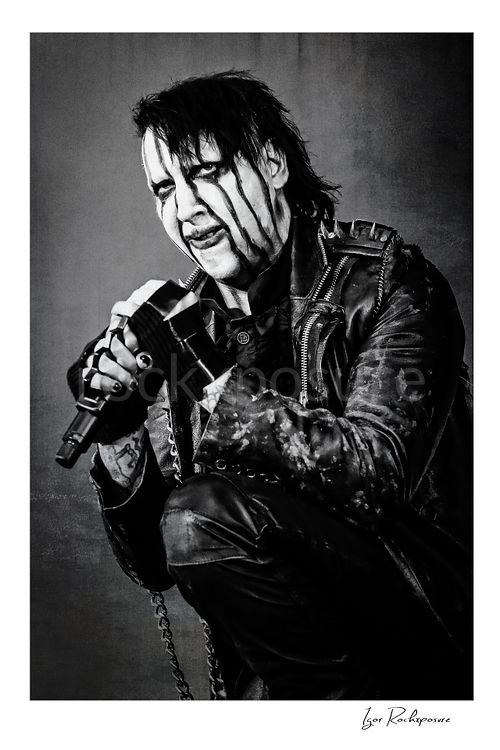 Vertical black and white image of Marilyn Manson holding a microphone in a tight theatrical portrait