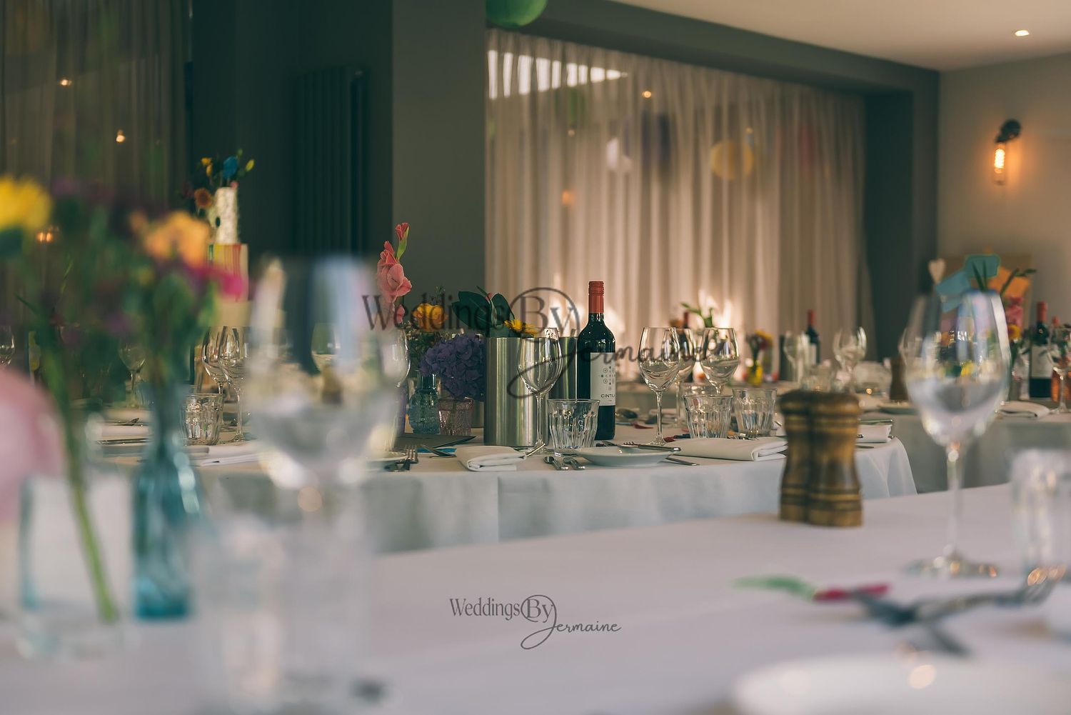 Distant view of wedding reception tables with the wedding cake in the background, photographed by Weddings by Jermaine